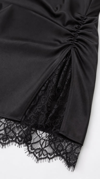 Close-up detail of side ruching and lace slit on black satin dress